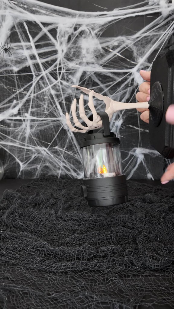 plastic skeleton hand on wooden base, holding a small lantern