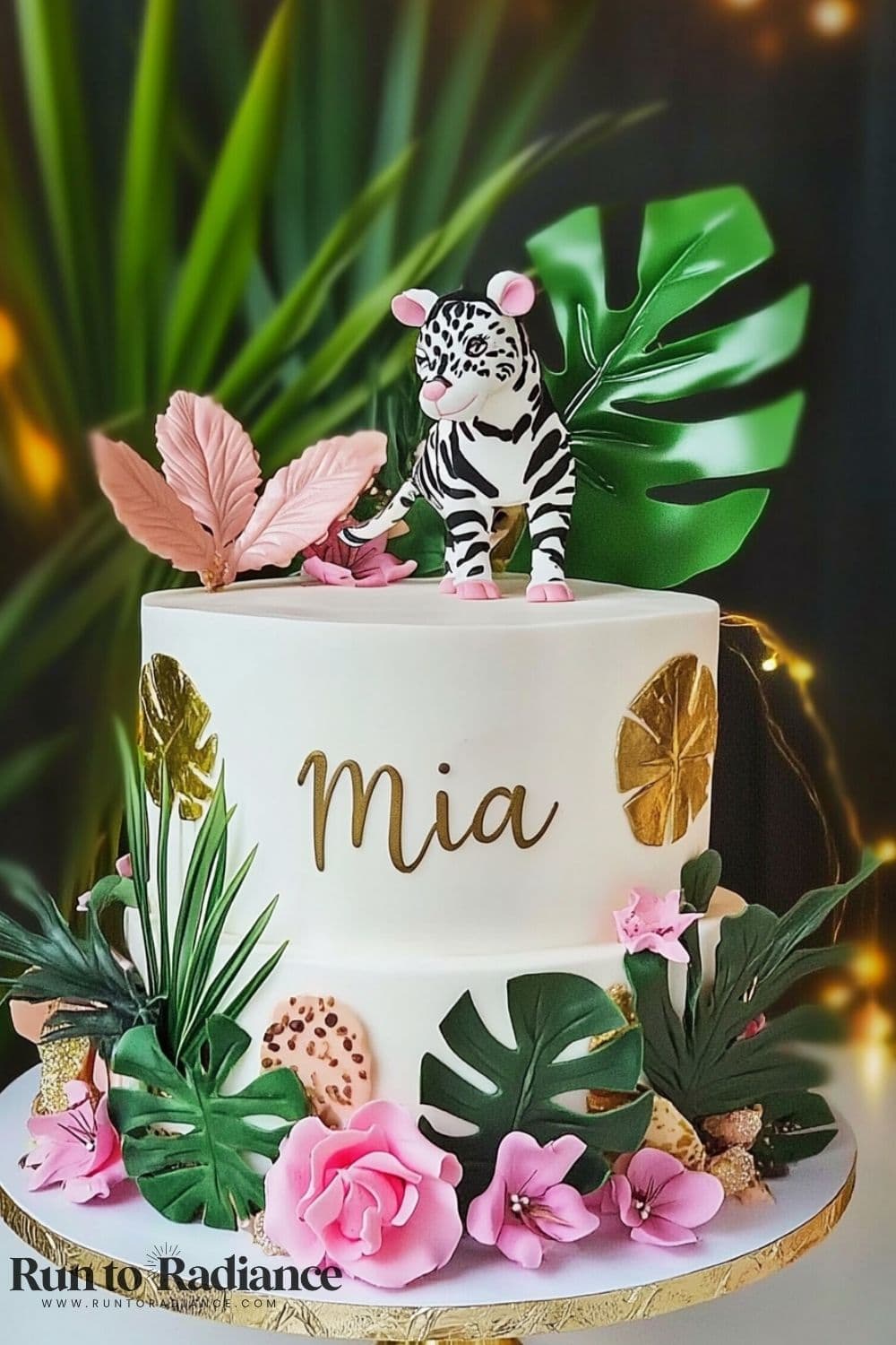 a zebra on top of a white cake with leaf embellishments and the name Mia in gold