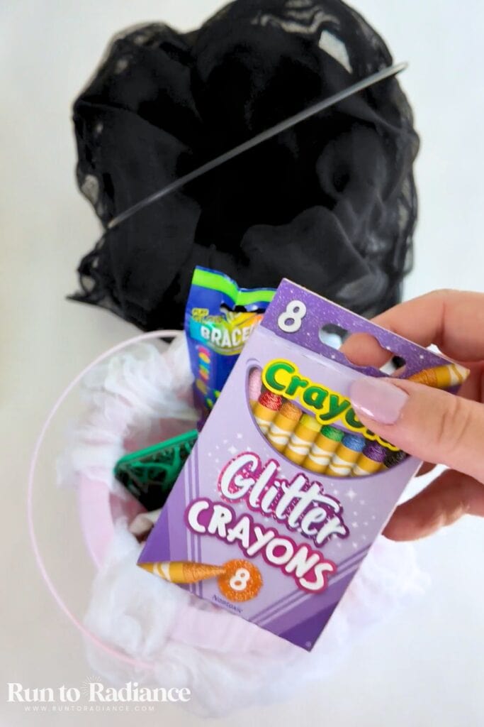 adding glitter crayons to a halloween boo basket