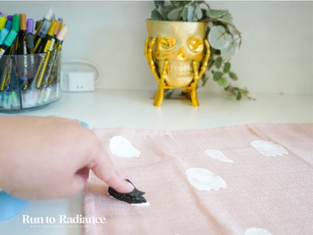 painting a pink pillow with white ghosts