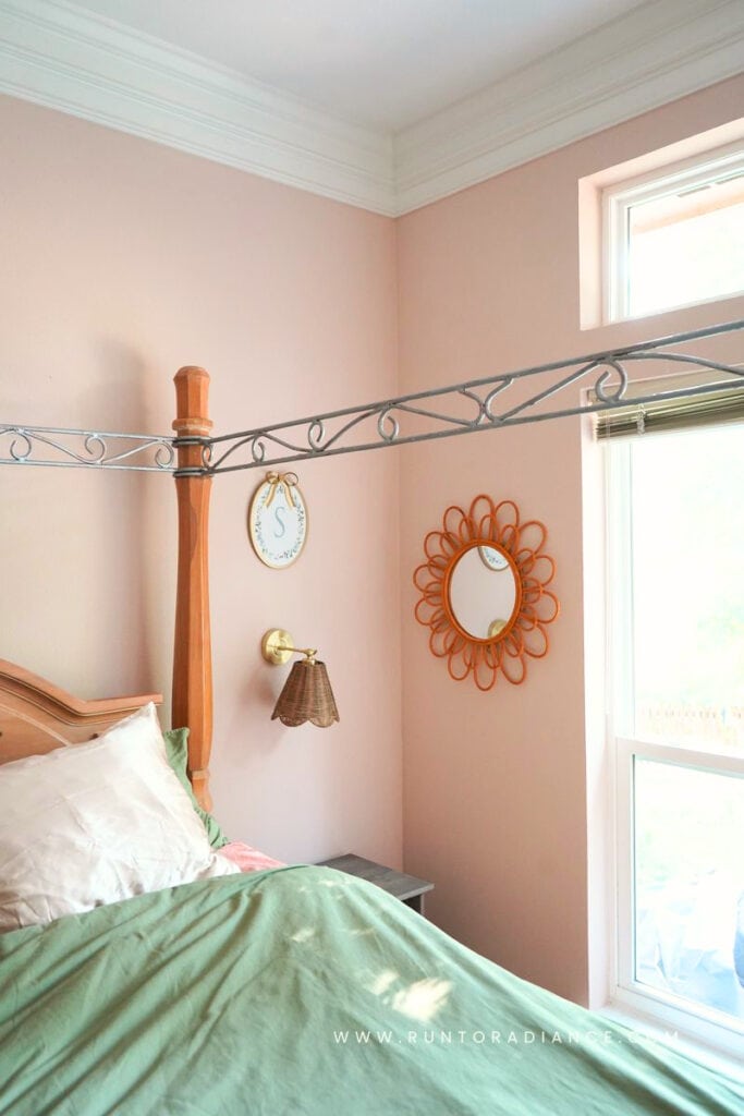 Pink cottagecore bedroom corner with a four-poster bed and rattan sunburst mirror