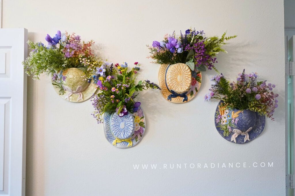 Cottagecore wall decor - 4 ceramic hat vases with wildflowers in them hanging on a wall.
