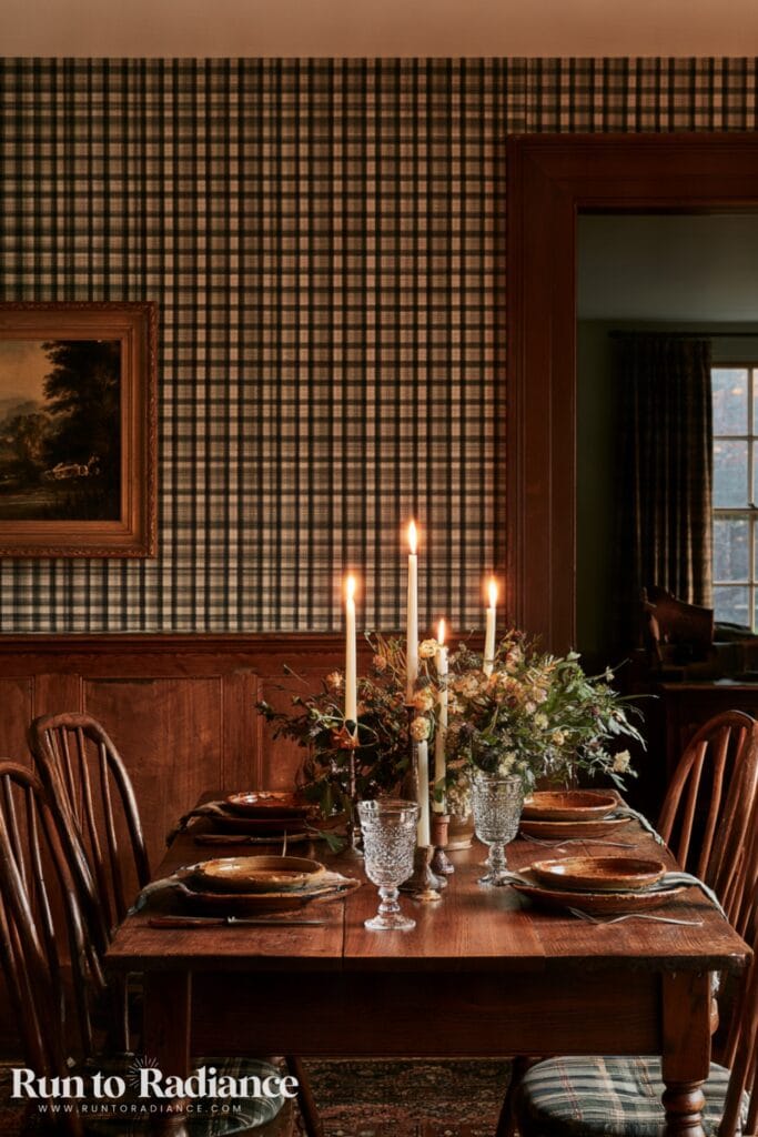 Dark cottagecore dining room at night with plaid wallpaper, solid wood wainscoting, fresh flowers, and lit candles.