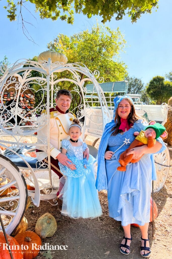 Family posing in Cinderella costumes beside a pumpkin carriage outdoors