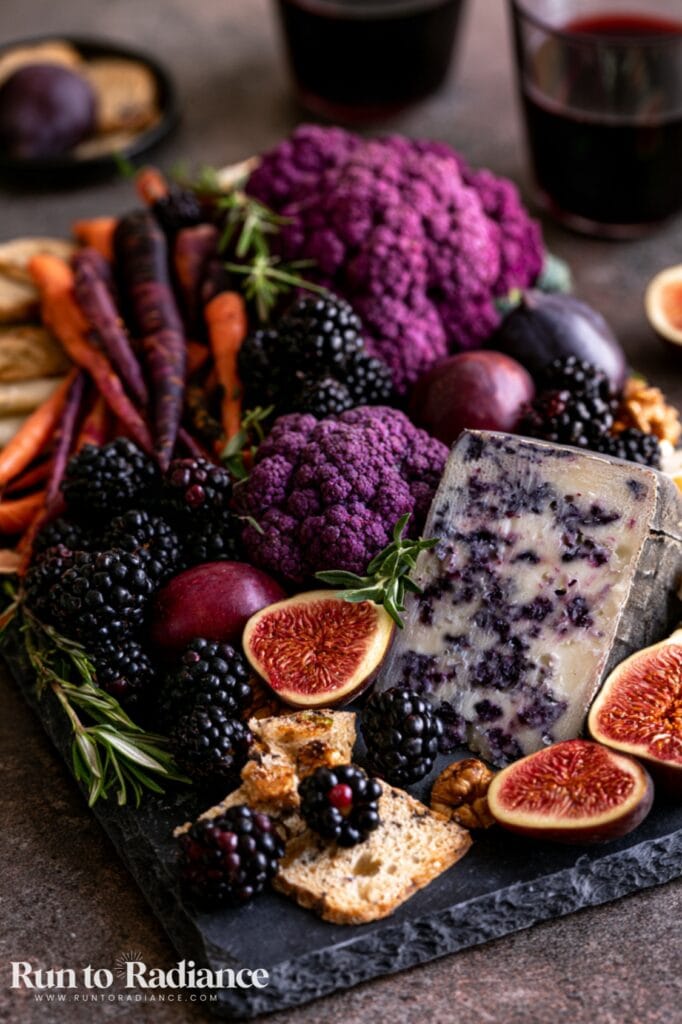 Halloween charcuterie board with blue cheese, purple cauliflower, figs, and blackberries on a slate board
