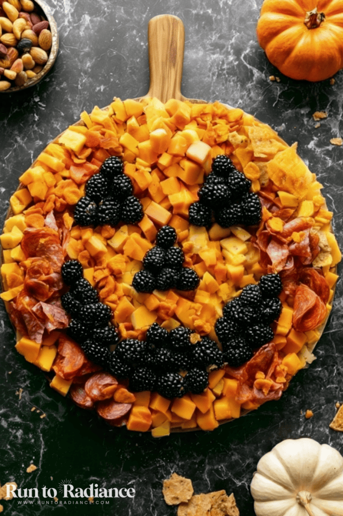 Halloween charcuterie board shaped like a jack-o-lantern with a blackberry face on cheese and meat