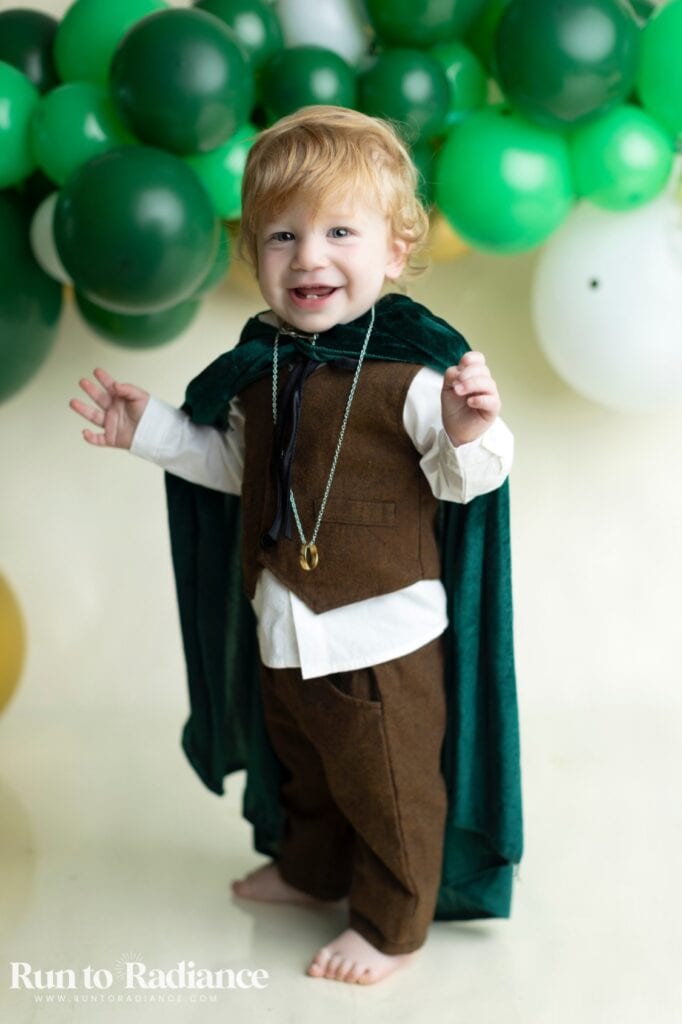 Toddler dressed as Frodo Baggins with brown vest green cape and ring necklace